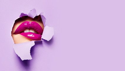 Naklejka premium Piękne pulchne jasne usta różowego koloru zaglądają w szczelinę kolorowego papieru.