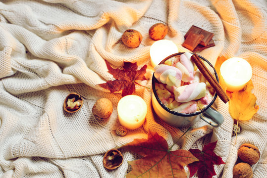 Toned Autumn made of dried fall leaves, mug of cocoa with marshmellows, nuts, cinnamon, candles on beige plaid