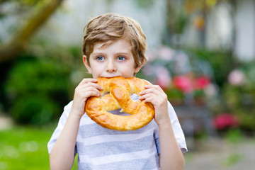 Adorable little kid boy eating huge big bavarian german pretzel.