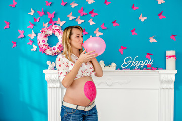 Happy pregnant woman blowing balloon against the backdrop of a blue wall with pink butterflies. Concept happy family