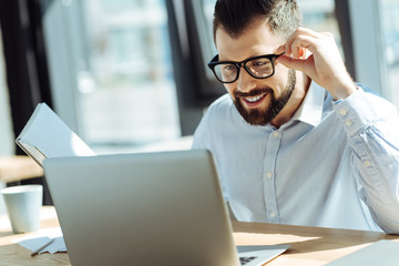 Smiling man looking at laptop while holding notebook