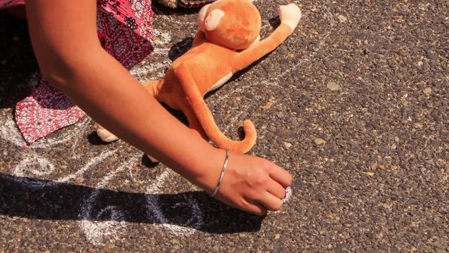 Young Girl Squats Draws with Chalk Picture on Asphalt by Toys
