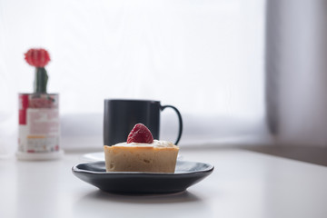 Fototapeta na wymiar A strawberry cheese tart , a black cup of hot coffee and cactus on white vintage wooden table and curtain background in minimalism cafe