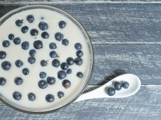 Yogurt with blueberries in a glass container stands on a wooden table.