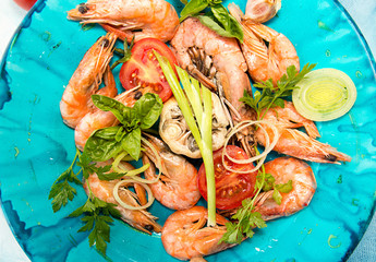 Bbq grilled shrimps on blue plate serving with cherry tomato, parsley, basil, leek and baked garlic. Barbecue seefood concept. Healthy diet food. Top view.