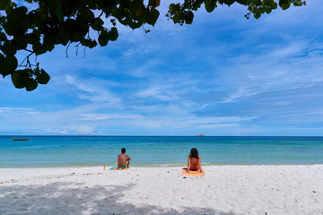 Young man and woman sunbathing on the beach, with sea-sky background.