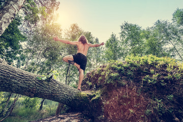 Young man standing on a tree trunk in the forest.