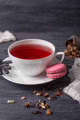 Fruit tea in a white cup and pink raspberry macaron on black background