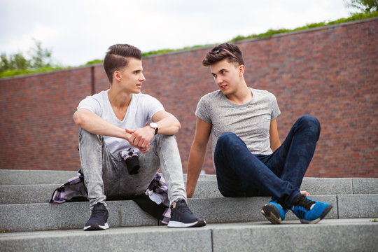 Two friends casual wear sitting on stairs in town and talking, best friend