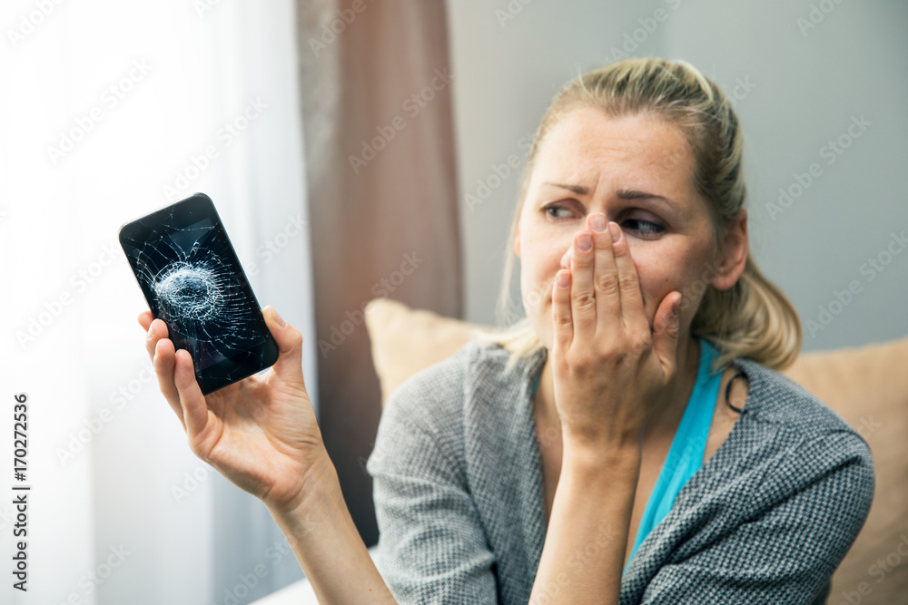 Wall mural sad woman holding smart phone with broken screen in hand