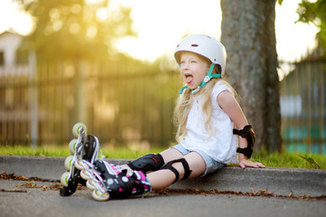 Pretty little girl learning to roller skate on beautiful summer day in a park