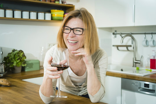 Senior woman in kitchen drinking red wine