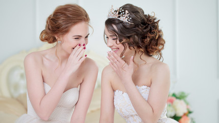 Two brides are whispering about something and laughing. Beautiful delicate Girls in wedding dresses.