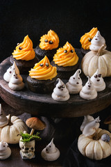 Fototapeta na wymiar Halloween decorated sweet dessert table black cupcake with orange cream, white meringue ghosts with chocolate eyes, decor skulls and pumpkin over black tablecloth.