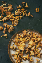 Heap of fresh uncooked forest mushrooms chanterelle in old pan over dark gray texture background. Top view with space