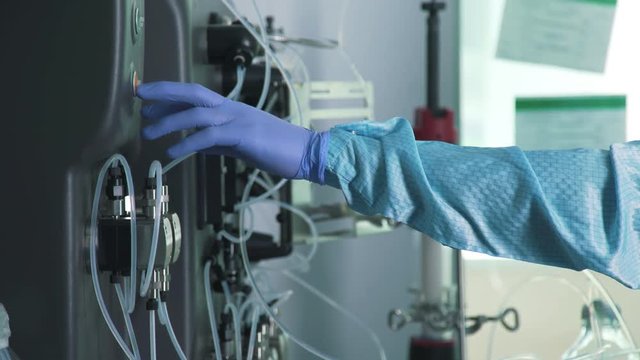 Hands of scientist in sterile blue protective gloves: laboratory assistant with chemical equipment. Work in scientific laboratory: control over the course of experiment and chemical reactions.