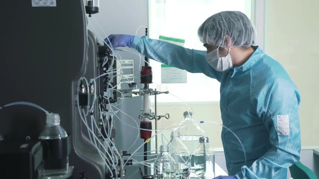 Scientist in a sterile suit (cap, face mask, latex gloves) makes manipulations in chemical laboratory. Laboratory assistant in chemical protection suit works with equipment. Science, biochemistry