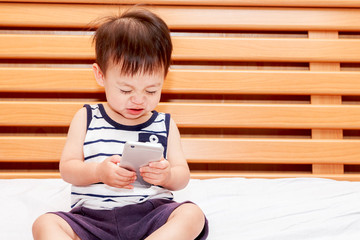 Baby boy holding smartphone on bed