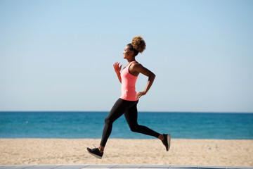 Full length healthy african woman running along the beach in morning