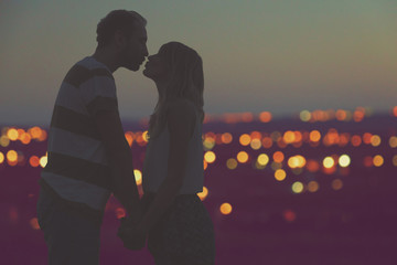 Silhouettes of a young couple kissing with city panorama in the background.