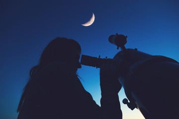 Naklejka premium Girl looking at the Moon through a telescope.