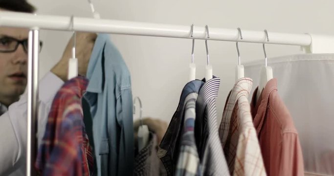 The young man changes his shirts on the hangers in the wardrobe.