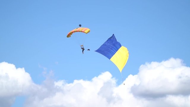 A parachutist with a huge flag of Ukraine descends on a yellow orange parachute