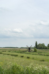 One small black mill in the green grass field under the cloudy sky in the day in the Netherlands
