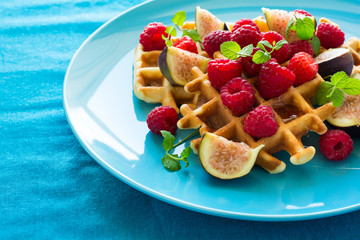 Healthy breakfast: Belgian waffles with raspberries, honey and figs decorated mint leaves on turquoise napkin. Selective focus. Close up