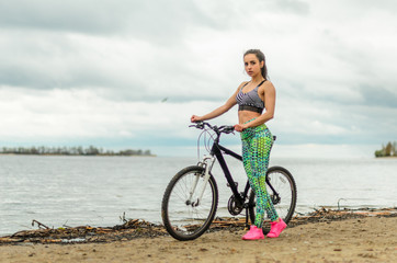 Fototapeta premium The girl the brunette plays sports on the seashore - on the beach. Rides a bike.