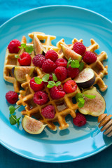 Healthy breakfast: Belgian waffles with raspberries, honey and figs decorated mint leaves on turquoise napkin. Selective focus. Close up