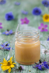 Obraz na płótnie Canvas raw organic royal jelly in a small bottle with litte spoon on small bottle surrounded by flowers