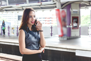 Young woman holding smartphone and standing at train station