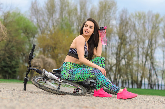 brunette girl in sportswear, riding a Bicycle in the morning in the Park. Resting and drinking water .