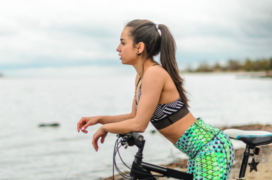 The girl the brunette plays sports on the seashore - on the beach. Rides a bike.