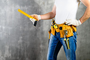 unidentified handyman standing with a tool belt with construction tools and holding roulette...