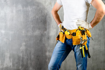 unknown handyman with hands on waist and tool belt with construction tools against grey background with copyspace for text. DIY tools and manual work concept