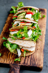 Pita sandwiches stuffed with chicken, vegetables and cheese on wooden cutting board