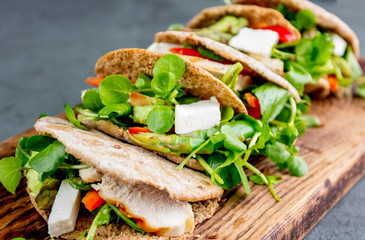 Pita sandwiches stuffed with chicken, vegetables and cheese on wooden cutting board