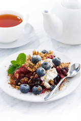 berry crumble with oat flakes, cream and blueberries for breakfast on table, closeup