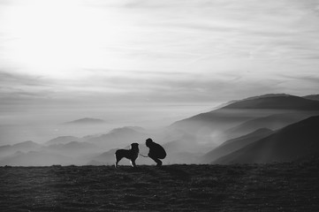 Silhouette di un uomo assieme al suo cane in un passaggio montuoso immerso nella nebbia 