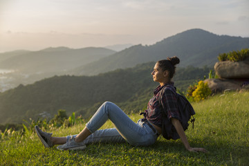 Naklejka na ściany i meble Hipster young girl with backpack enjoying sunset on peak mountain. Tourist traveler on background valley landscape view mockup.