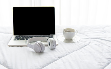 The laptop working on the white bed and coffee in the sunny day morning holiday.  Lifestyle Concept. soft and select focus