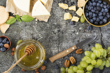 Cheese board for snacks, tricks, meetings with friends, on a gray stone background: assorted cheeses, young cheese, parmesan, cheese with fenugreek, figs, nuts, honey, grapes. Top View.