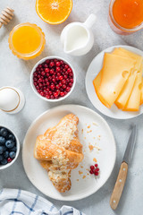 Continental breakfast table top view. Fresh croissants, boiled egg, cheese, orange, jam, honey, cream, blueberries and currants on bright blue table. Vertical