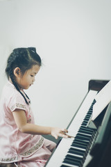 Cute little asian girl in traditional chinese dress playing piano with one hand. Digital color filter.