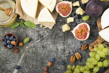 Cheese board for snacks, tricks, meetings with friends, on a gray stone background: assorted cheeses, young cheese, parmesan, cheese with fenugreek, figs, nuts, honey, grapes. Top View.