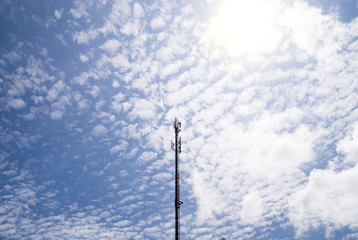 Mobile phone and communications tower with cloud and blue sky.