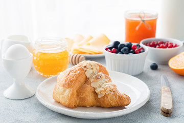 Almond croissant, honey, fresh blueberries, orange, jam, currants, boiled egg and bottle of milk on table . Closeup view of continental breakfast. Copy space