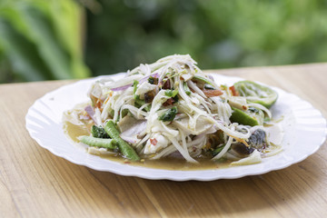 Papaya salad in a white dish on wooden floor